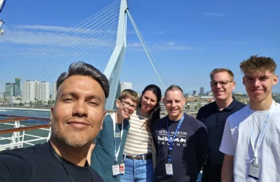 Cruising with Danny and Peter, Holland America Line, Nieuw Statendam, Rotterdam, The Netherlands, Voyage Rotterdam Nieuw Statendam Embarkation | A vibrant collage capturing embarkation day on Holland America’s Nieuw Statendam docked at Rotterdam’s Cruise Terminal, with the Erasmus Bridge and Zalmhaventoren in the background under a golden afternoon sky. The ship’s elegant atrium sparkles with a chandelier, while a cozy Oceanview Family Cabin showcases bunk beds and large windows framing the Nieuwe Maas. A family tours the Lido Market, where tables overflow with herb-crusted lamb, chocolate eggs, and colorful desserts for Easter lunch. On deck, two teenagers snap selfies against Rotterdam’s twinkling skyline during sail away, the ship gliding past the illuminated Swan Bridge. In the Ocean Bar, friends toast with cocktails, and the Crow’s Nest lounge offers panoramic views of the river. The scene closes with a cozy cabin moment, a TV glowing with Formula 1 action, hot chocolate mugs on a table, and the gentle sway of the ship at dusk.