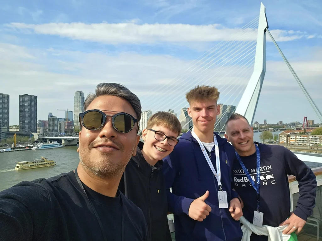 Rotterdam Cruise Port: Our Complete Guide + Insider Tips 2026 (Visited 5 Times Since 2022 by Danny and Peter) 13 Cruising with Danny and Peter, Holland America Line, Nieuw Statendam, Rotterdam, The Netherlands, Voyage Rotterdam Nieuw Statendam Embarkation | A vibrant collage capturing embarkation day on Holland America’s Nieuw Statendam docked at Rotterdam’s Cruise Terminal, with the Erasmus Bridge and Zalmhaventoren in the background under a golden afternoon sky. The ship’s elegant atrium sparkles with a chandelier, while a cozy Oceanview Family Cabin showcases bunk beds and large windows framing the Nieuwe Maas. A family tours the Lido Market, where tables overflow with herb-crusted lamb, chocolate eggs, and colorful desserts for Easter lunch. On deck, two teenagers snap selfies against Rotterdam’s twinkling skyline during sail away, the ship gliding past the illuminated Swan Bridge. In the Ocean Bar, friends toast with cocktails, and the Crow’s Nest lounge offers panoramic views of the river. The scene closes with a cozy cabin moment, a TV glowing with Formula 1 action, hot chocolate mugs on a table, and the gentle sway of the ship at dusk.