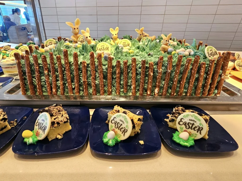 Rotterdam Cruise Port: Our Complete Guide + Insider Tips 2026 (Visited 5 Times Since 2022 by Danny and Peter) 5 Cruising with Danny and Peter, Holland America Line, Nieuw Statendam, Rotterdam, The Netherlands, Voyage Rotterdam Nieuw Statendam Embarkation | A vibrant collage capturing embarkation day on Holland America’s Nieuw Statendam docked at Rotterdam’s Cruise Terminal, with the Erasmus Bridge and Zalmhaventoren in the background under a golden afternoon sky. The ship’s elegant atrium sparkles with a chandelier, while a cozy Oceanview Family Cabin showcases bunk beds and large windows framing the Nieuwe Maas. A family tours the Lido Market, where tables overflow with herb-crusted lamb, chocolate eggs, and colorful desserts for Easter lunch. On deck, two teenagers snap selfies against Rotterdam’s twinkling skyline during sail away, the ship gliding past the illuminated Swan Bridge. In the Ocean Bar, friends toast with cocktails, and the Crow’s Nest lounge offers panoramic views of the river. The scene closes with a cozy cabin moment, a TV glowing with Formula 1 action, hot chocolate mugs on a table, and the gentle sway of the ship at dusk.