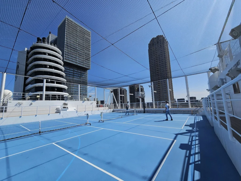 Rotterdam Cruise Port: Our Complete Guide + Insider Tips 2026 (Visited 5 Times Since 2022 by Danny and Peter) 7 Cruising with Danny and Peter, Holland America Line, Nieuw Statendam, Rotterdam, The Netherlands, Voyage Rotterdam Nieuw Statendam Embarkation | A vibrant collage capturing embarkation day on Holland America’s Nieuw Statendam docked at Rotterdam’s Cruise Terminal, with the Erasmus Bridge and Zalmhaventoren in the background under a golden afternoon sky. The ship’s elegant atrium sparkles with a chandelier, while a cozy Oceanview Family Cabin showcases bunk beds and large windows framing the Nieuwe Maas. A family tours the Lido Market, where tables overflow with herb-crusted lamb, chocolate eggs, and colorful desserts for Easter lunch. On deck, two teenagers snap selfies against Rotterdam’s twinkling skyline during sail away, the ship gliding past the illuminated Swan Bridge. In the Ocean Bar, friends toast with cocktails, and the Crow’s Nest lounge offers panoramic views of the river. The scene closes with a cozy cabin moment, a TV glowing with Formula 1 action, hot chocolate mugs on a table, and the gentle sway of the ship at dusk.