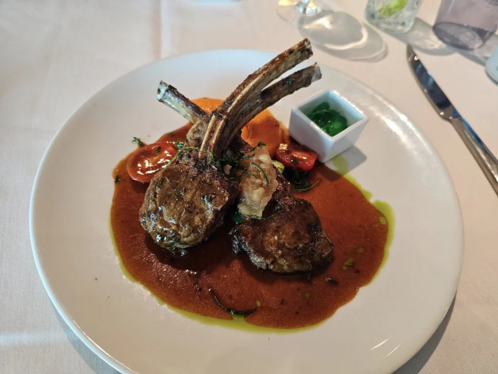 Rotterdam Cruise Port: Our Complete Guide + Insider Tips 2026 (Visited 5 Times Since 2022 by Danny and Peter) 24 Cruising with Danny and Peter, Holland America Line, Nieuw Statendam, Rotterdam, The Netherlands, Voyage Rotterdam Nieuw Statendam Embarkation | A vibrant collage capturing embarkation day on Holland America’s Nieuw Statendam docked at Rotterdam’s Cruise Terminal, with the Erasmus Bridge and Zalmhaventoren in the background under a golden afternoon sky. The ship’s elegant atrium sparkles with a chandelier, while a cozy Oceanview Family Cabin showcases bunk beds and large windows framing the Nieuwe Maas. A family tours the Lido Market, where tables overflow with herb-crusted lamb, chocolate eggs, and colorful desserts for Easter lunch. On deck, two teenagers snap selfies against Rotterdam’s twinkling skyline during sail away, the ship gliding past the illuminated Swan Bridge. In the Ocean Bar, friends toast with cocktails, and the Crow’s Nest lounge offers panoramic views of the river. The scene closes with a cozy cabin moment, a TV glowing with Formula 1 action, hot chocolate mugs on a table, and the gentle sway of the ship at dusk.