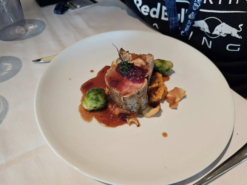 Rotterdam Cruise Port: Our Complete Guide + Insider Tips 2026 (Visited 5 Times Since 2022 by Danny and Peter) 25 Cruising with Danny and Peter, Holland America Line, Nieuw Statendam, Rotterdam, The Netherlands, Voyage Rotterdam Nieuw Statendam Embarkation | A vibrant collage capturing embarkation day on Holland America’s Nieuw Statendam docked at Rotterdam’s Cruise Terminal, with the Erasmus Bridge and Zalmhaventoren in the background under a golden afternoon sky. The ship’s elegant atrium sparkles with a chandelier, while a cozy Oceanview Family Cabin showcases bunk beds and large windows framing the Nieuwe Maas. A family tours the Lido Market, where tables overflow with herb-crusted lamb, chocolate eggs, and colorful desserts for Easter lunch. On deck, two teenagers snap selfies against Rotterdam’s twinkling skyline during sail away, the ship gliding past the illuminated Swan Bridge. In the Ocean Bar, friends toast with cocktails, and the Crow’s Nest lounge offers panoramic views of the river. The scene closes with a cozy cabin moment, a TV glowing with Formula 1 action, hot chocolate mugs on a table, and the gentle sway of the ship at dusk.