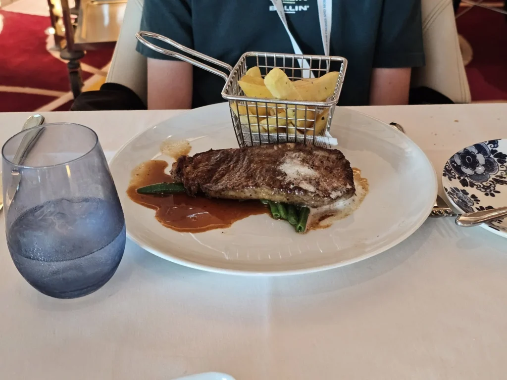 Rotterdam Cruise Port: Our Complete Guide + Insider Tips 2026 (Visited 5 Times Since 2022 by Danny and Peter) 8 Cruising with Danny and Peter, Holland America Line, Nieuw Statendam, Rotterdam, The Netherlands, Voyage Rotterdam Nieuw Statendam Embarkation | A vibrant collage capturing embarkation day on Holland America’s Nieuw Statendam docked at Rotterdam’s Cruise Terminal, with the Erasmus Bridge and Zalmhaventoren in the background under a golden afternoon sky. The ship’s elegant atrium sparkles with a chandelier, while a cozy Oceanview Family Cabin showcases bunk beds and large windows framing the Nieuwe Maas. A family tours the Lido Market, where tables overflow with herb-crusted lamb, chocolate eggs, and colorful desserts for Easter lunch. On deck, two teenagers snap selfies against Rotterdam’s twinkling skyline during sail away, the ship gliding past the illuminated Swan Bridge. In the Ocean Bar, friends toast with cocktails, and the Crow’s Nest lounge offers panoramic views of the river. The scene closes with a cozy cabin moment, a TV glowing with Formula 1 action, hot chocolate mugs on a table, and the gentle sway of the ship at dusk.