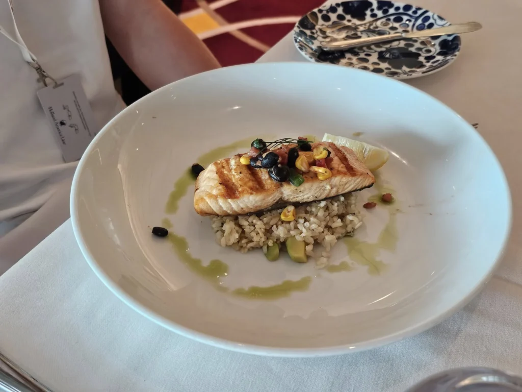 Rotterdam Cruise Port: Our Complete Guide + Insider Tips 2026 (Visited 5 Times Since 2022 by Danny and Peter) 9 Cruising with Danny and Peter, Holland America Line, Nieuw Statendam, Rotterdam, The Netherlands, Voyage Rotterdam Nieuw Statendam Embarkation | A vibrant collage capturing embarkation day on Holland America’s Nieuw Statendam docked at Rotterdam’s Cruise Terminal, with the Erasmus Bridge and Zalmhaventoren in the background under a golden afternoon sky. The ship’s elegant atrium sparkles with a chandelier, while a cozy Oceanview Family Cabin showcases bunk beds and large windows framing the Nieuwe Maas. A family tours the Lido Market, where tables overflow with herb-crusted lamb, chocolate eggs, and colorful desserts for Easter lunch. On deck, two teenagers snap selfies against Rotterdam’s twinkling skyline during sail away, the ship gliding past the illuminated Swan Bridge. In the Ocean Bar, friends toast with cocktails, and the Crow’s Nest lounge offers panoramic views of the river. The scene closes with a cozy cabin moment, a TV glowing with Formula 1 action, hot chocolate mugs on a table, and the gentle sway of the ship at dusk.