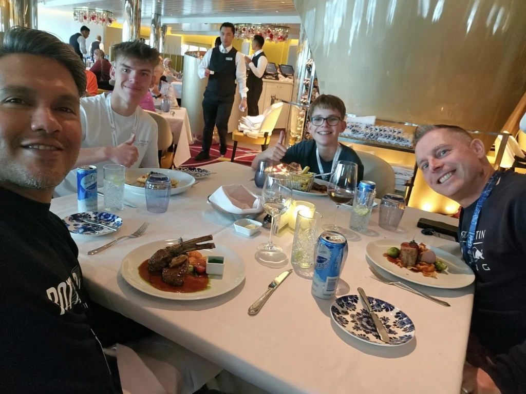 Rotterdam Cruise Port: Our Complete Guide + Insider Tips 2026 (Visited 5 Times Since 2022 by Danny and Peter) 10 Cruising with Danny and Peter, Holland America Line, Nieuw Statendam, Rotterdam, The Netherlands, Voyage Rotterdam Nieuw Statendam Embarkation | A vibrant collage capturing embarkation day on Holland America’s Nieuw Statendam docked at Rotterdam’s Cruise Terminal, with the Erasmus Bridge and Zalmhaventoren in the background under a golden afternoon sky. The ship’s elegant atrium sparkles with a chandelier, while a cozy Oceanview Family Cabin showcases bunk beds and large windows framing the Nieuwe Maas. A family tours the Lido Market, where tables overflow with herb-crusted lamb, chocolate eggs, and colorful desserts for Easter lunch. On deck, two teenagers snap selfies against Rotterdam’s twinkling skyline during sail away, the ship gliding past the illuminated Swan Bridge. In the Ocean Bar, friends toast with cocktails, and the Crow’s Nest lounge offers panoramic views of the river. The scene closes with a cozy cabin moment, a TV glowing with Formula 1 action, hot chocolate mugs on a table, and the gentle sway of the ship at dusk.