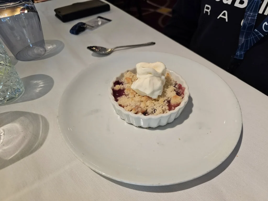 Rotterdam Cruise Port: Our Complete Guide + Insider Tips 2026 (Visited 5 Times Since 2022 by Danny and Peter) 26 Cruising with Danny and Peter, Holland America Line, Nieuw Statendam, Rotterdam, The Netherlands, Voyage Rotterdam Nieuw Statendam Embarkation | A vibrant collage capturing embarkation day on Holland America’s Nieuw Statendam docked at Rotterdam’s Cruise Terminal, with the Erasmus Bridge and Zalmhaventoren in the background under a golden afternoon sky. The ship’s elegant atrium sparkles with a chandelier, while a cozy Oceanview Family Cabin showcases bunk beds and large windows framing the Nieuwe Maas. A family tours the Lido Market, where tables overflow with herb-crusted lamb, chocolate eggs, and colorful desserts for Easter lunch. On deck, two teenagers snap selfies against Rotterdam’s twinkling skyline during sail away, the ship gliding past the illuminated Swan Bridge. In the Ocean Bar, friends toast with cocktails, and the Crow’s Nest lounge offers panoramic views of the river. The scene closes with a cozy cabin moment, a TV glowing with Formula 1 action, hot chocolate mugs on a table, and the gentle sway of the ship at dusk.