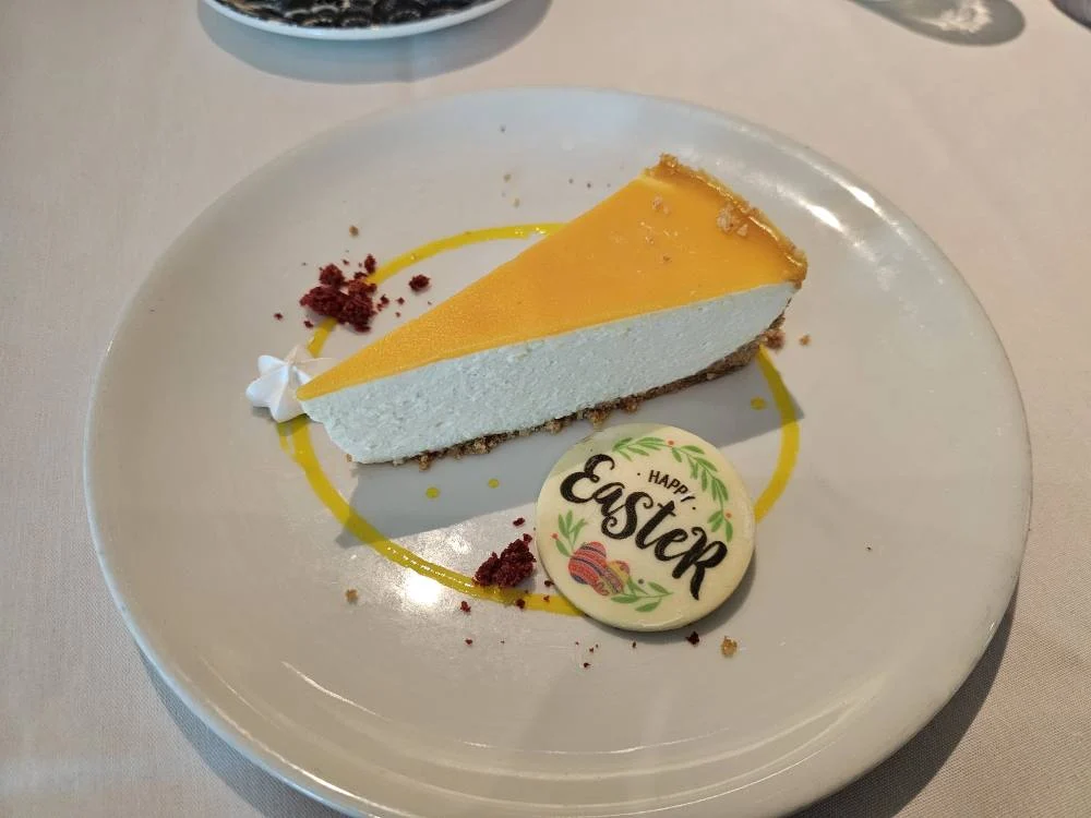 Rotterdam Cruise Port: Our Complete Guide + Insider Tips 2026 (Visited 5 Times Since 2022 by Danny and Peter) 27 Cruising with Danny and Peter, Holland America Line, Nieuw Statendam, Rotterdam, The Netherlands, Voyage Rotterdam Nieuw Statendam Embarkation | A vibrant collage capturing embarkation day on Holland America’s Nieuw Statendam docked at Rotterdam’s Cruise Terminal, with the Erasmus Bridge and Zalmhaventoren in the background under a golden afternoon sky. The ship’s elegant atrium sparkles with a chandelier, while a cozy Oceanview Family Cabin showcases bunk beds and large windows framing the Nieuwe Maas. A family tours the Lido Market, where tables overflow with herb-crusted lamb, chocolate eggs, and colorful desserts for Easter lunch. On deck, two teenagers snap selfies against Rotterdam’s twinkling skyline during sail away, the ship gliding past the illuminated Swan Bridge. In the Ocean Bar, friends toast with cocktails, and the Crow’s Nest lounge offers panoramic views of the river. The scene closes with a cozy cabin moment, a TV glowing with Formula 1 action, hot chocolate mugs on a table, and the gentle sway of the ship at dusk.