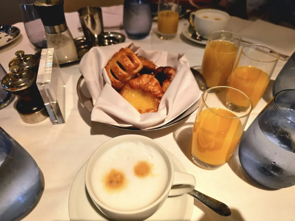 A Voyage Through Time and Tide: Exploring the English Channel Aboard Holland America Line’s Nieuw Statendam 2 Cruising with Danny and Peter, Holland America Line, Nieuw Statendam, English Channel, Sea Day, English Channel Nieuw Statendam Sea Day Experience | A luxurious scene aboard Holland America Line’s Nieuw Statendam cruising the English Channel, featuring the Main Dining Room with elegantly set tables, gourmet dishes like eggs Benedict, and large windows revealing gray-green waves; the intimate Pinnacle Grill with plush seating and a plated beef tenderloin with lobster dumplings; the World Stage theater’s circular stage and vibrant 270-degree LED screen displaying Casablanca’s Hassan II Mosque; and the ship’s sleek white hull sailing smoothly under an overcast sky, embodying modern cruising elegance.