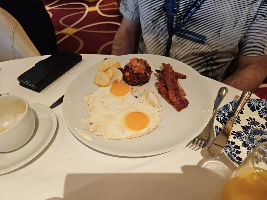 A Voyage Through Time and Tide: Exploring the English Channel Aboard Holland America Line’s Nieuw Statendam 4 Cruising with Danny and Peter, Holland America Line, Nieuw Statendam, English Channel, Sea Day, English Channel Nieuw Statendam Sea Day Experience | A luxurious scene aboard Holland America Line’s Nieuw Statendam cruising the English Channel, featuring the Main Dining Room with elegantly set tables, gourmet dishes like eggs Benedict, and large windows revealing gray-green waves; the intimate Pinnacle Grill with plush seating and a plated beef tenderloin with lobster dumplings; the World Stage theater’s circular stage and vibrant 270-degree LED screen displaying Casablanca’s Hassan II Mosque; and the ship’s sleek white hull sailing smoothly under an overcast sky, embodying modern cruising elegance.