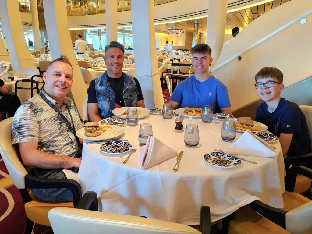 A Voyage Through Time and Tide: Exploring the English Channel Aboard Holland America Line’s Nieuw Statendam 5 Cruising with Danny and Peter, Holland America Line, Nieuw Statendam, English Channel, Sea Day, English Channel Nieuw Statendam Sea Day Experience | A luxurious scene aboard Holland America Line’s Nieuw Statendam cruising the English Channel, featuring the Main Dining Room with elegantly set tables, gourmet dishes like eggs Benedict, and large windows revealing gray-green waves; the intimate Pinnacle Grill with plush seating and a plated beef tenderloin with lobster dumplings; the World Stage theater’s circular stage and vibrant 270-degree LED screen displaying Casablanca’s Hassan II Mosque; and the ship’s sleek white hull sailing smoothly under an overcast sky, embodying modern cruising elegance.