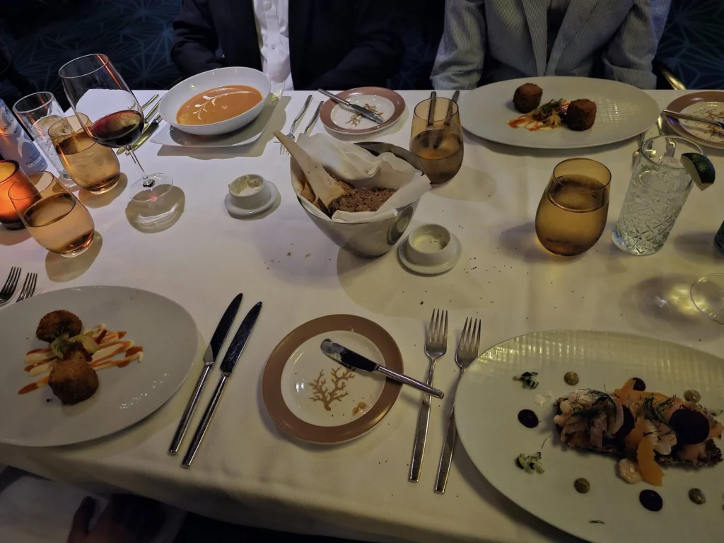 A Voyage Through Time and Tide: Exploring the English Channel Aboard Holland America Line’s Nieuw Statendam 27 Cruising with Danny and Peter, Holland America Line, Nieuw Statendam, English Channel, Sea Day, English Channel Nieuw Statendam Sea Day Experience | A luxurious scene aboard Holland America Line’s Nieuw Statendam cruising the English Channel, featuring the Main Dining Room with elegantly set tables, gourmet dishes like eggs Benedict, and large windows revealing gray-green waves; the intimate Pinnacle Grill with plush seating and a plated beef tenderloin with lobster dumplings; the World Stage theater’s circular stage and vibrant 270-degree LED screen displaying Casablanca’s Hassan II Mosque; and the ship’s sleek white hull sailing smoothly under an overcast sky, embodying modern cruising elegance.