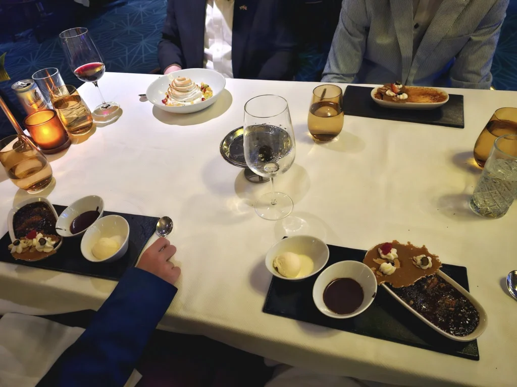 A Voyage Through Time and Tide: Exploring the English Channel Aboard Holland America Line’s Nieuw Statendam 35 Cruising with Danny and Peter, Holland America Line, Nieuw Statendam, English Channel, Sea Day, English Channel Nieuw Statendam Sea Day Experience | A luxurious scene aboard Holland America Line’s Nieuw Statendam cruising the English Channel, featuring the Main Dining Room with elegantly set tables, gourmet dishes like eggs Benedict, and large windows revealing gray-green waves; the intimate Pinnacle Grill with plush seating and a plated beef tenderloin with lobster dumplings; the World Stage theater’s circular stage and vibrant 270-degree LED screen displaying Casablanca’s Hassan II Mosque; and the ship’s sleek white hull sailing smoothly under an overcast sky, embodying modern cruising elegance.