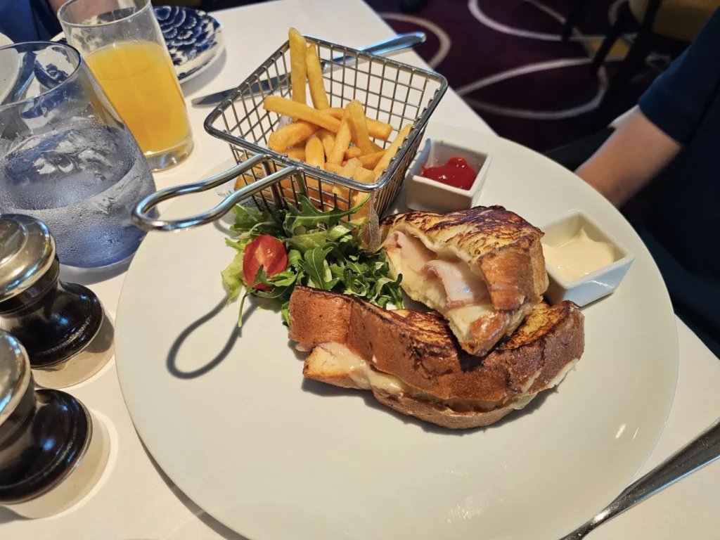 Cruising with Danny and Peter, Holland America Line, Nieuw Statendam, Bay Of Biscay History Sea Day | A scenic view of the Bay of Biscay’s deep blue waters under a partly cloudy sky, with gentle waves reflecting sunlight, alongside the elegant Dining Room of Holland America’s Nieuw Statendam, featuring white tablecloths, polished silverware, and a plate of lobster Benedict with hollandaise sauce. The World Stage theater showcases a vibrant LED screen displaying Agadir’s bustling souk with colorful spices and crafts, while the Lido Pool area glows at night with twinkling lights, where guests mingle with champagne during the Mariners Reception. The intimate Tamarind restaurant, with warm wood decor, presents a beautifully plated Penang red curry with duck, paired with a sake flight.