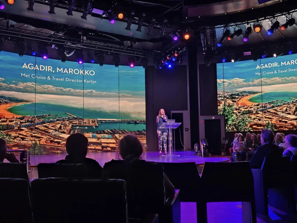 Cruising with Danny and Peter, Holland America Line, Nieuw Statendam, Bay Of Biscay History Sea Day | A scenic view of the Bay of Biscay’s deep blue waters under a partly cloudy sky, with gentle waves reflecting sunlight, alongside the elegant Dining Room of Holland America’s Nieuw Statendam, featuring white tablecloths, polished silverware, and a plate of lobster Benedict with hollandaise sauce. The World Stage theater showcases a vibrant LED screen displaying Agadir’s bustling souk with colorful spices and crafts, while the Lido Pool area glows at night with twinkling lights, where guests mingle with champagne during the Mariners Reception. The intimate Tamarind restaurant, with warm wood decor, presents a beautifully plated Penang red curry with duck, paired with a sake flight.