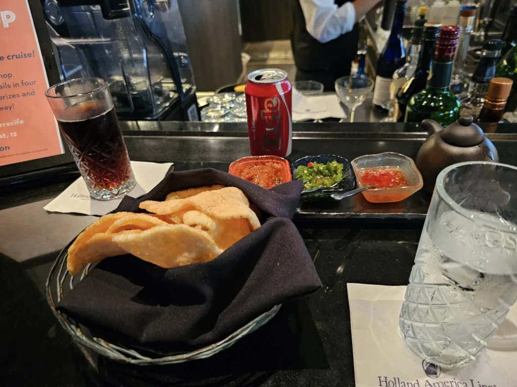 Cruising with Danny and Peter, Holland America Line, Nieuw Statendam, Bay Of Biscay History Sea Day | A scenic view of the Bay of Biscay’s deep blue waters under a partly cloudy sky, with gentle waves reflecting sunlight, alongside the elegant Dining Room of Holland America’s Nieuw Statendam, featuring white tablecloths, polished silverware, and a plate of lobster Benedict with hollandaise sauce. The World Stage theater showcases a vibrant LED screen displaying Agadir’s bustling souk with colorful spices and crafts, while the Lido Pool area glows at night with twinkling lights, where guests mingle with champagne during the Mariners Reception. The intimate Tamarind restaurant, with warm wood decor, presents a beautifully plated Penang red curry with duck, paired with a sake flight.