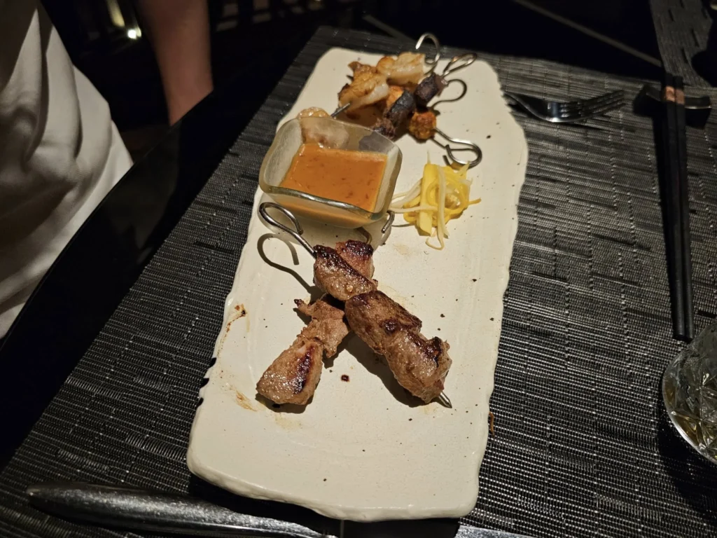 Cruising with Danny and Peter, Holland America Line, Nieuw Statendam, Bay Of Biscay History Sea Day | A scenic view of the Bay of Biscay’s deep blue waters under a partly cloudy sky, with gentle waves reflecting sunlight, alongside the elegant Dining Room of Holland America’s Nieuw Statendam, featuring white tablecloths, polished silverware, and a plate of lobster Benedict with hollandaise sauce. The World Stage theater showcases a vibrant LED screen displaying Agadir’s bustling souk with colorful spices and crafts, while the Lido Pool area glows at night with twinkling lights, where guests mingle with champagne during the Mariners Reception. The intimate Tamarind restaurant, with warm wood decor, presents a beautifully plated Penang red curry with duck, paired with a sake flight.