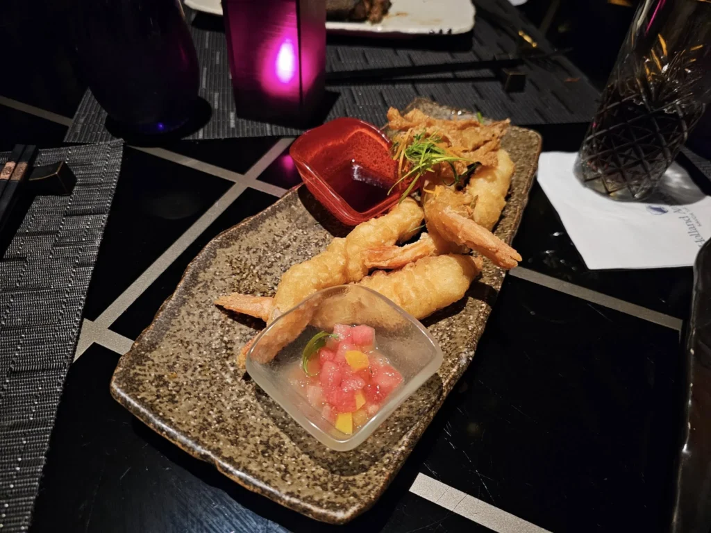 Cruising with Danny and Peter, Holland America Line, Nieuw Statendam, Bay Of Biscay History Sea Day | A scenic view of the Bay of Biscay’s deep blue waters under a partly cloudy sky, with gentle waves reflecting sunlight, alongside the elegant Dining Room of Holland America’s Nieuw Statendam, featuring white tablecloths, polished silverware, and a plate of lobster Benedict with hollandaise sauce. The World Stage theater showcases a vibrant LED screen displaying Agadir’s bustling souk with colorful spices and crafts, while the Lido Pool area glows at night with twinkling lights, where guests mingle with champagne during the Mariners Reception. The intimate Tamarind restaurant, with warm wood decor, presents a beautifully plated Penang red curry with duck, paired with a sake flight.