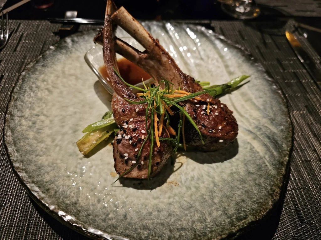 Cruising with Danny and Peter, Holland America Line, Nieuw Statendam, Bay Of Biscay History Sea Day | A scenic view of the Bay of Biscay’s deep blue waters under a partly cloudy sky, with gentle waves reflecting sunlight, alongside the elegant Dining Room of Holland America’s Nieuw Statendam, featuring white tablecloths, polished silverware, and a plate of lobster Benedict with hollandaise sauce. The World Stage theater showcases a vibrant LED screen displaying Agadir’s bustling souk with colorful spices and crafts, while the Lido Pool area glows at night with twinkling lights, where guests mingle with champagne during the Mariners Reception. The intimate Tamarind restaurant, with warm wood decor, presents a beautifully plated Penang red curry with duck, paired with a sake flight.