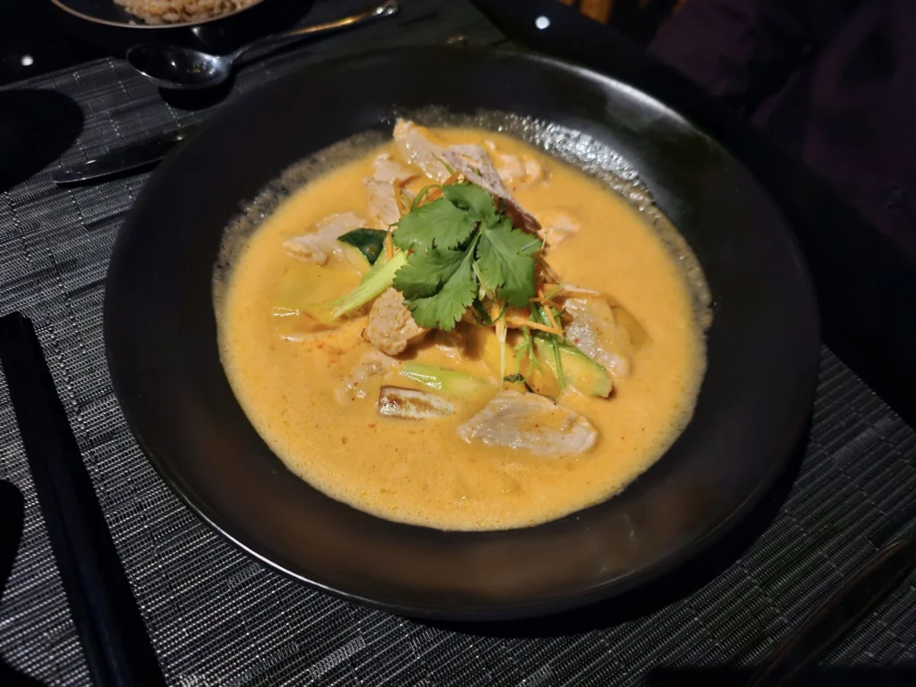 Cruising with Danny and Peter, Holland America Line, Nieuw Statendam, Bay Of Biscay History Sea Day | A scenic view of the Bay of Biscay’s deep blue waters under a partly cloudy sky, with gentle waves reflecting sunlight, alongside the elegant Dining Room of Holland America’s Nieuw Statendam, featuring white tablecloths, polished silverware, and a plate of lobster Benedict with hollandaise sauce. The World Stage theater showcases a vibrant LED screen displaying Agadir’s bustling souk with colorful spices and crafts, while the Lido Pool area glows at night with twinkling lights, where guests mingle with champagne during the Mariners Reception. The intimate Tamarind restaurant, with warm wood decor, presents a beautifully plated Penang red curry with duck, paired with a sake flight.