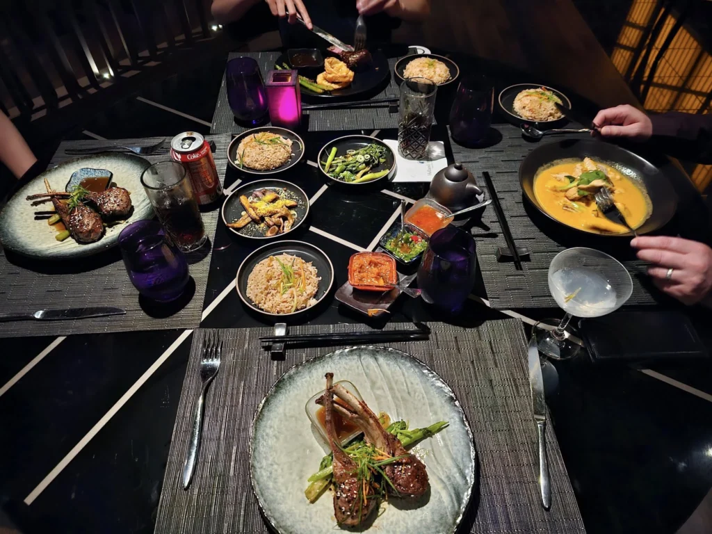 Cruising with Danny and Peter, Holland America Line, Nieuw Statendam, Bay Of Biscay History Sea Day | A scenic view of the Bay of Biscay’s deep blue waters under a partly cloudy sky, with gentle waves reflecting sunlight, alongside the elegant Dining Room of Holland America’s Nieuw Statendam, featuring white tablecloths, polished silverware, and a plate of lobster Benedict with hollandaise sauce. The World Stage theater showcases a vibrant LED screen displaying Agadir’s bustling souk with colorful spices and crafts, while the Lido Pool area glows at night with twinkling lights, where guests mingle with champagne during the Mariners Reception. The intimate Tamarind restaurant, with warm wood decor, presents a beautifully plated Penang red curry with duck, paired with a sake flight.