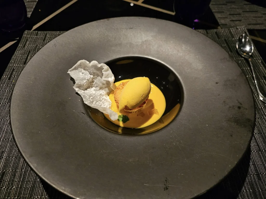 Cruising with Danny and Peter, Holland America Line, Nieuw Statendam, Bay Of Biscay History Sea Day | A scenic view of the Bay of Biscay’s deep blue waters under a partly cloudy sky, with gentle waves reflecting sunlight, alongside the elegant Dining Room of Holland America’s Nieuw Statendam, featuring white tablecloths, polished silverware, and a plate of lobster Benedict with hollandaise sauce. The World Stage theater showcases a vibrant LED screen displaying Agadir’s bustling souk with colorful spices and crafts, while the Lido Pool area glows at night with twinkling lights, where guests mingle with champagne during the Mariners Reception. The intimate Tamarind restaurant, with warm wood decor, presents a beautifully plated Penang red curry with duck, paired with a sake flight.