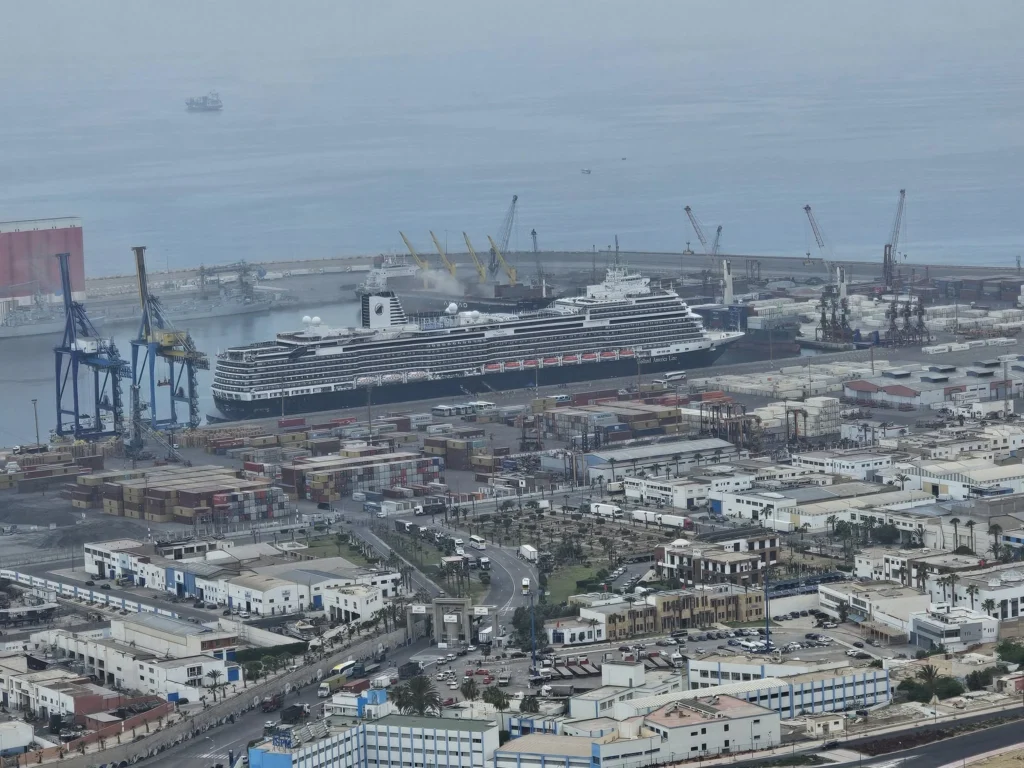 Cruising with Danny and Peter, Holland America Line, Nieuw Statendam, Agadir Morocco Adventure | A vibrant collage capturing a day in Agadir, Morocco, during a Holland America Nieuw Statendam cruise: the white façade and green-tiled minaret of Mosque Mohammed V gleaming under the sun; the bustling Agadir Marina with yachts bobbing in the harbor and golden beach sands stretching toward the Anti-Atlas Mountains; the historic Agadir Oufella kasbah ruins on a hill overlooking the sparkling Atlantic; Sven riding a camel along a scenic path with a Berber handler; the colorful chaos of Souk El Had market with stalls of spices, rugs, and jewelry; the lush Paradise Valley oasis with palm trees, clear pools, and tiny fish nibbling at feet; and an aromatic garden with Moroccan bread, argan oil, and mint tea under a shaded canopy.