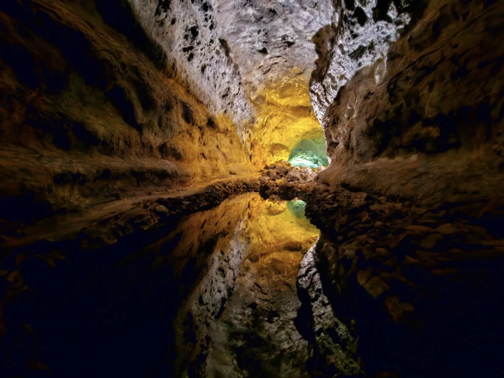 Cruising with Danny and Peter, Holland America Line, Nieuw Statendam, Arrecife, Lanzarote, Canary Islands, Volcanic Adventure | A vibrant collage capturing an adventure in Arrecife, Lanzarote: the dark, winding lava tunnels of Cueva de los Verdes illuminated by soft lights; the serene turquoise pool and lush greenery of Jameos del Agua with its volcanic cave backdrop; the sweeping ocean views from Mirador del Río’s cliffside lookout, framing La Graciosa island; and the surreal, Mars-like red and black lava fields of Timanfaya National Park under a clear sky, showcasing Lanzarote’s volcanic beauty.