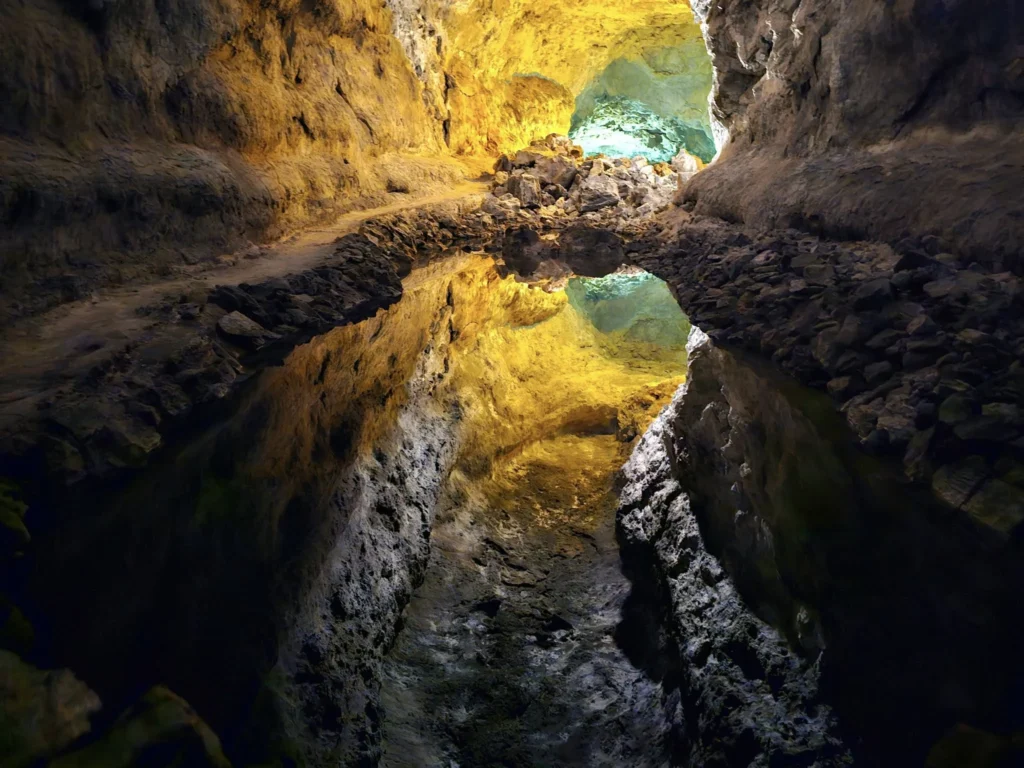 Cruising with Danny and Peter, Holland America Line, Nieuw Statendam, Arrecife, Lanzarote, Canary Islands, Volcanic Adventure | A vibrant collage capturing an adventure in Arrecife, Lanzarote: the dark, winding lava tunnels of Cueva de los Verdes illuminated by soft lights; the serene turquoise pool and lush greenery of Jameos del Agua with its volcanic cave backdrop; the sweeping ocean views from Mirador del Río’s cliffside lookout, framing La Graciosa island; and the surreal, Mars-like red and black lava fields of Timanfaya National Park under a clear sky, showcasing Lanzarote’s volcanic beauty.