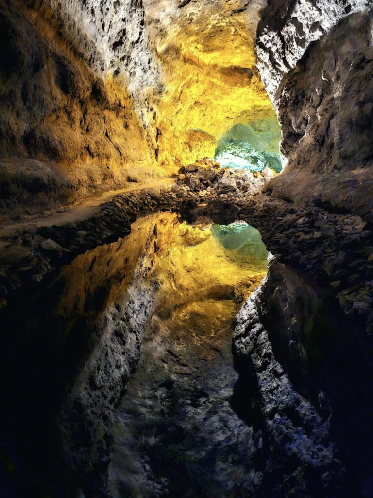 Cruising with Danny and Peter, Holland America Line, Nieuw Statendam, Arrecife, Lanzarote, Canary Islands, Volcanic Adventure | A vibrant collage capturing an adventure in Arrecife, Lanzarote: the dark, winding lava tunnels of Cueva de los Verdes illuminated by soft lights; the serene turquoise pool and lush greenery of Jameos del Agua with its volcanic cave backdrop; the sweeping ocean views from Mirador del Río’s cliffside lookout, framing La Graciosa island; and the surreal, Mars-like red and black lava fields of Timanfaya National Park under a clear sky, showcasing Lanzarote’s volcanic beauty.