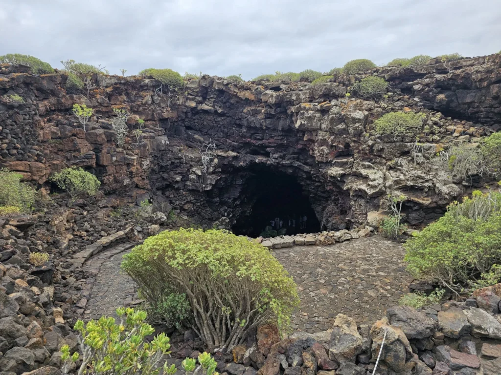 Cruising with Danny and Peter, Holland America Line, Nieuw Statendam, Arrecife, Lanzarote, Canary Islands, Volcanic Adventure | A vibrant collage capturing an adventure in Arrecife, Lanzarote: the dark, winding lava tunnels of Cueva de los Verdes illuminated by soft lights; the serene turquoise pool and lush greenery of Jameos del Agua with its volcanic cave backdrop; the sweeping ocean views from Mirador del Río’s cliffside lookout, framing La Graciosa island; and the surreal, Mars-like red and black lava fields of Timanfaya National Park under a clear sky, showcasing Lanzarote’s volcanic beauty.