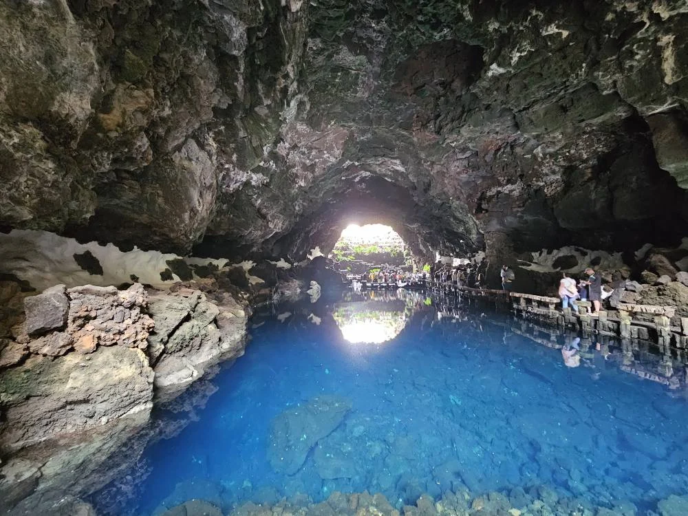 Cruising with Danny and Peter, Holland America Line, Nieuw Statendam, Arrecife, Lanzarote, Canary Islands, Volcanic Adventure | A vibrant collage capturing an adventure in Arrecife, Lanzarote: the dark, winding lava tunnels of Cueva de los Verdes illuminated by soft lights; the serene turquoise pool and lush greenery of Jameos del Agua with its volcanic cave backdrop; the sweeping ocean views from Mirador del Río’s cliffside lookout, framing La Graciosa island; and the surreal, Mars-like red and black lava fields of Timanfaya National Park under a clear sky, showcasing Lanzarote’s volcanic beauty.