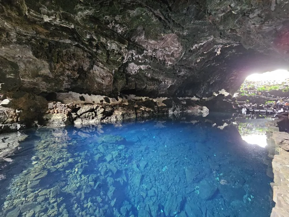 Cruising with Danny and Peter, Holland America Line, Nieuw Statendam, Arrecife, Lanzarote, Canary Islands, Volcanic Adventure | A vibrant collage capturing an adventure in Arrecife, Lanzarote: the dark, winding lava tunnels of Cueva de los Verdes illuminated by soft lights; the serene turquoise pool and lush greenery of Jameos del Agua with its volcanic cave backdrop; the sweeping ocean views from Mirador del Río’s cliffside lookout, framing La Graciosa island; and the surreal, Mars-like red and black lava fields of Timanfaya National Park under a clear sky, showcasing Lanzarote’s volcanic beauty.