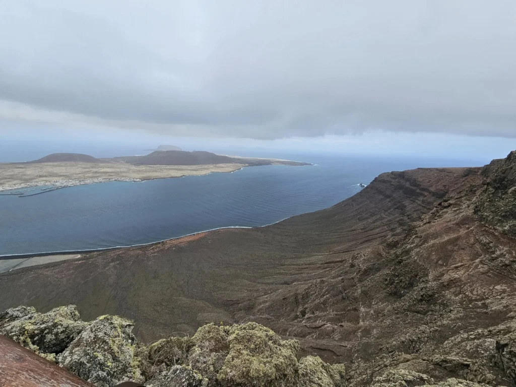 Cruising with Danny and Peter, Holland America Line, Nieuw Statendam, Arrecife, Lanzarote, Canary Islands, Volcanic Adventure | A vibrant collage capturing an adventure in Arrecife, Lanzarote: the dark, winding lava tunnels of Cueva de los Verdes illuminated by soft lights; the serene turquoise pool and lush greenery of Jameos del Agua with its volcanic cave backdrop; the sweeping ocean views from Mirador del Río’s cliffside lookout, framing La Graciosa island; and the surreal, Mars-like red and black lava fields of Timanfaya National Park under a clear sky, showcasing Lanzarote’s volcanic beauty.