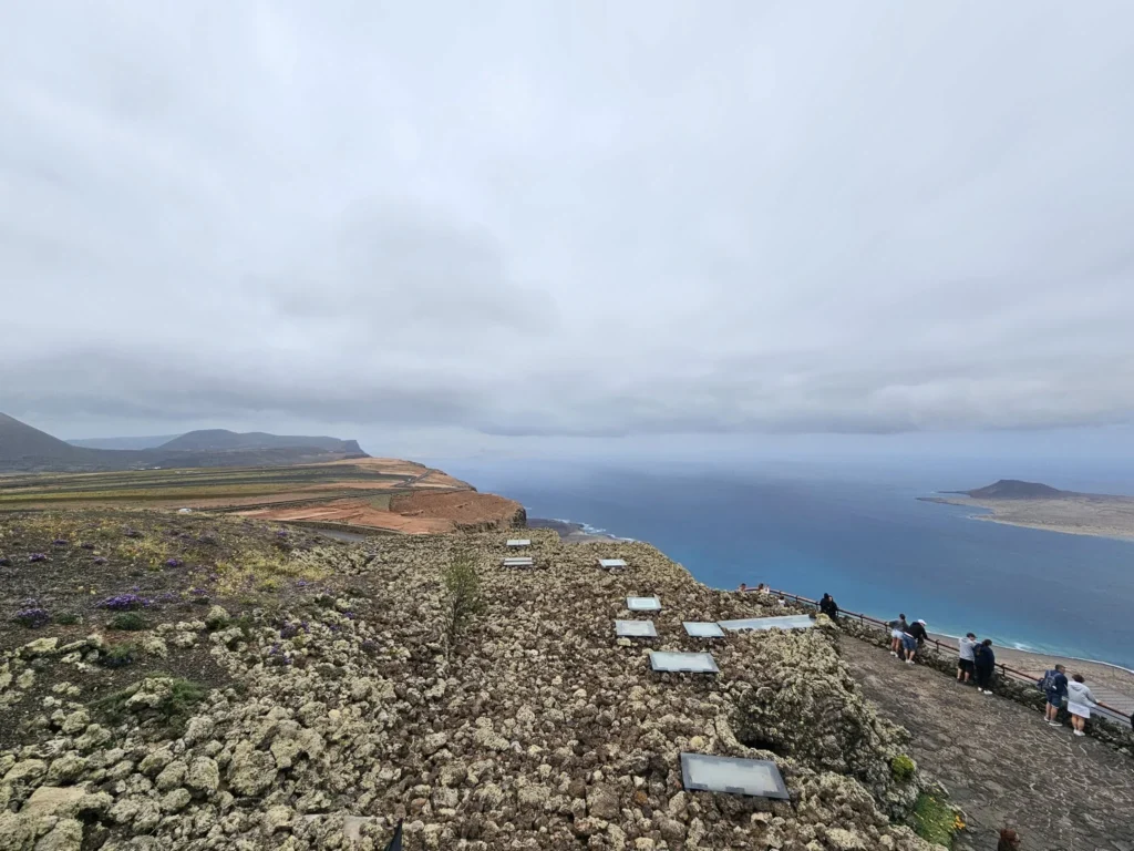 Cruising with Danny and Peter, Holland America Line, Nieuw Statendam, Arrecife, Lanzarote, Canary Islands, Volcanic Adventure | A vibrant collage capturing an adventure in Arrecife, Lanzarote: the dark, winding lava tunnels of Cueva de los Verdes illuminated by soft lights; the serene turquoise pool and lush greenery of Jameos del Agua with its volcanic cave backdrop; the sweeping ocean views from Mirador del Río’s cliffside lookout, framing La Graciosa island; and the surreal, Mars-like red and black lava fields of Timanfaya National Park under a clear sky, showcasing Lanzarote’s volcanic beauty.