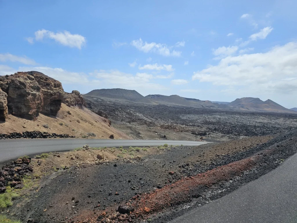 Cruising with Danny and Peter, Holland America Line, Nieuw Statendam, Arrecife, Lanzarote, Canary Islands, Volcanic Adventure | A vibrant collage capturing an adventure in Arrecife, Lanzarote: the dark, winding lava tunnels of Cueva de los Verdes illuminated by soft lights; the serene turquoise pool and lush greenery of Jameos del Agua with its volcanic cave backdrop; the sweeping ocean views from Mirador del Río’s cliffside lookout, framing La Graciosa island; and the surreal, Mars-like red and black lava fields of Timanfaya National Park under a clear sky, showcasing Lanzarote’s volcanic beauty.
