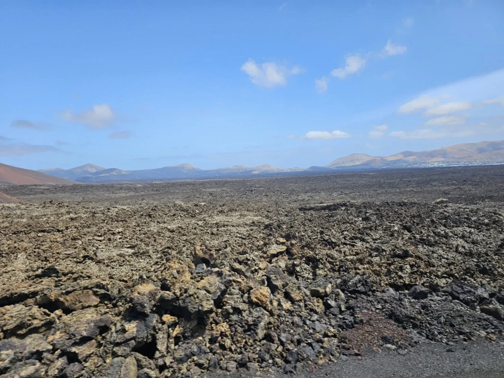 Cruising with Danny and Peter, Holland America Line, Nieuw Statendam, Arrecife, Lanzarote, Canary Islands, Volcanic Adventure | A vibrant collage capturing an adventure in Arrecife, Lanzarote: the dark, winding lava tunnels of Cueva de los Verdes illuminated by soft lights; the serene turquoise pool and lush greenery of Jameos del Agua with its volcanic cave backdrop; the sweeping ocean views from Mirador del Río’s cliffside lookout, framing La Graciosa island; and the surreal, Mars-like red and black lava fields of Timanfaya National Park under a clear sky, showcasing Lanzarote’s volcanic beauty.
