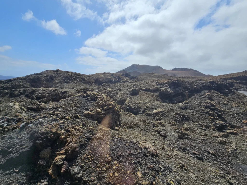 Cruising with Danny and Peter, Holland America Line, Nieuw Statendam, Arrecife, Lanzarote, Canary Islands, Volcanic Adventure | A vibrant collage capturing an adventure in Arrecife, Lanzarote: the dark, winding lava tunnels of Cueva de los Verdes illuminated by soft lights; the serene turquoise pool and lush greenery of Jameos del Agua with its volcanic cave backdrop; the sweeping ocean views from Mirador del Río’s cliffside lookout, framing La Graciosa island; and the surreal, Mars-like red and black lava fields of Timanfaya National Park under a clear sky, showcasing Lanzarote’s volcanic beauty.