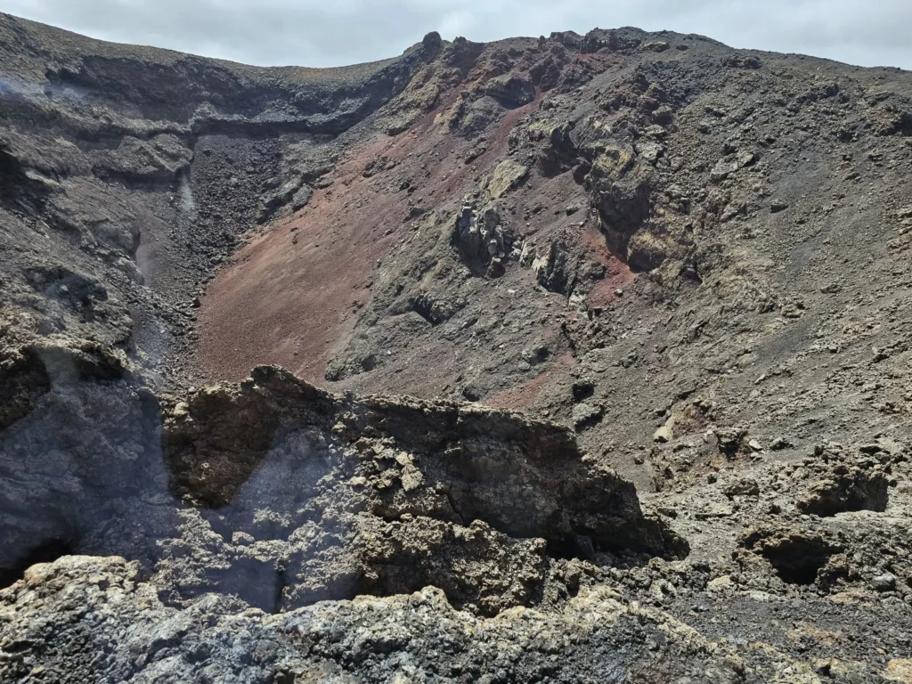 Cruising with Danny and Peter, Holland America Line, Nieuw Statendam, Arrecife, Lanzarote, Canary Islands, Volcanic Adventure | A vibrant collage capturing an adventure in Arrecife, Lanzarote: the dark, winding lava tunnels of Cueva de los Verdes illuminated by soft lights; the serene turquoise pool and lush greenery of Jameos del Agua with its volcanic cave backdrop; the sweeping ocean views from Mirador del Río’s cliffside lookout, framing La Graciosa island; and the surreal, Mars-like red and black lava fields of Timanfaya National Park under a clear sky, showcasing Lanzarote’s volcanic beauty.
