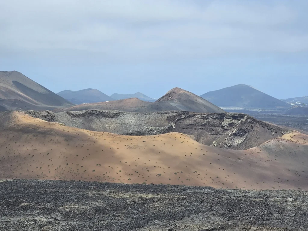 Cruising with Danny and Peter, Holland America Line, Nieuw Statendam, Arrecife, Lanzarote, Canary Islands, Volcanic Adventure | A vibrant collage capturing an adventure in Arrecife, Lanzarote: the dark, winding lava tunnels of Cueva de los Verdes illuminated by soft lights; the serene turquoise pool and lush greenery of Jameos del Agua with its volcanic cave backdrop; the sweeping ocean views from Mirador del Río’s cliffside lookout, framing La Graciosa island; and the surreal, Mars-like red and black lava fields of Timanfaya National Park under a clear sky, showcasing Lanzarote’s volcanic beauty.