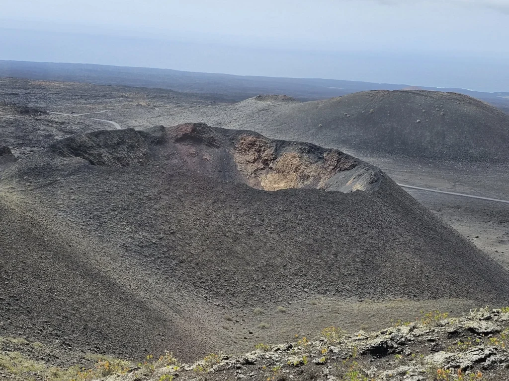 Cruising with Danny and Peter, Holland America Line, Nieuw Statendam, Arrecife, Lanzarote, Canary Islands, Volcanic Adventure | A vibrant collage capturing an adventure in Arrecife, Lanzarote: the dark, winding lava tunnels of Cueva de los Verdes illuminated by soft lights; the serene turquoise pool and lush greenery of Jameos del Agua with its volcanic cave backdrop; the sweeping ocean views from Mirador del Río’s cliffside lookout, framing La Graciosa island; and the surreal, Mars-like red and black lava fields of Timanfaya National Park under a clear sky, showcasing Lanzarote’s volcanic beauty.