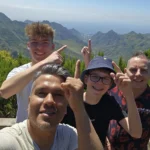 Cruising with Danny and Peter, Holland America Line, Nieuw Statendam, Santa Cruz, Tenerife, Canary Islands, History Adventure | A vibrant collage capturing Santa Cruz, Tenerife’s diverse beauty: the misty, lush laurel forests of Anaga Rural Park with sunlight filtering through dense green foliage at Mirador Cruz del Carmen; a panoramic view from Mirador Pico del Inglés showcasing rugged Anaga Mountains and the distant Atlantic Ocean under a partly cloudy sky; the golden sands of Playa de las Teresitas lined with palm trees and calm turquoise waters; a colorful seafood platter with grilled prawns and papas arrugadas served at a beachfront restaurant; and the elegant Nieuw Statendam cruise ship docked at Santa Cruz port with the city’s skyline and Anaga Mountains in the background.