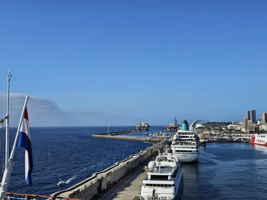 Cruising with Danny and Peter, Holland America Line, Nieuw Statendam, Santa Cruz, Tenerife, Canary Islands, History Adventure | A vibrant collage capturing Santa Cruz, Tenerife’s diverse beauty: the misty, lush laurel forests of Anaga Rural Park with sunlight filtering through dense green foliage at Mirador Cruz del Carmen; a panoramic view from Mirador Pico del Inglés showcasing rugged Anaga Mountains and the distant Atlantic Ocean under a partly cloudy sky; the golden sands of Playa de las Teresitas lined with palm trees and calm turquoise waters; a colorful seafood platter with grilled prawns and papas arrugadas served at a beachfront restaurant; and the elegant Nieuw Statendam cruise ship docked at Santa Cruz port with the city’s skyline and Anaga Mountains in the background.