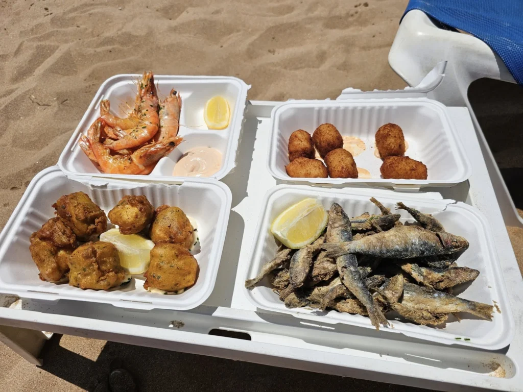 Cruising with Danny and Peter, Holland America Line, Nieuw Statendam, Santa Cruz, Tenerife, Canary Islands, History Adventure | A vibrant collage capturing Santa Cruz, Tenerife’s diverse beauty: the misty, lush laurel forests of Anaga Rural Park with sunlight filtering through dense green foliage at Mirador Cruz del Carmen; a panoramic view from Mirador Pico del Inglés showcasing rugged Anaga Mountains and the distant Atlantic Ocean under a partly cloudy sky; the golden sands of Playa de las Teresitas lined with palm trees and calm turquoise waters; a colorful seafood platter with grilled prawns and papas arrugadas served at a beachfront restaurant; and the elegant Nieuw Statendam cruise ship docked at Santa Cruz port with the city’s skyline and Anaga Mountains in the background.