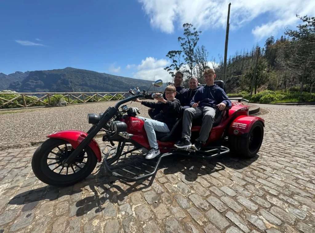 Cruising with Danny and Peter, Holland America Line, Nieuw Statendam, Funchal, Madeira. Portugal, History Adventure | A vibrant collage capturing a day in Funchal, Madeira: a sleek trike navigates winding roads with lush green hills in the background; the panoramic view from Pico dos Barcelos showcases Funchal Bay and the Desertas Islands under a clear sky; Cascata dos Anjos waterfall cascades from cliffs onto a road, surrounded by verdant greenery; Praia da Madalena do Mar’s pebbled beach and black volcanic sand meet gentle waves with towering cliffs above; the misty Valley of the Nuns nestles between rugged mountains, dotted with stone houses and chestnut groves; Cabo Girão’s glass-bottomed skywalk reveals a dizzying drop to the Atlantic and terraced fields below; a plate of warm bolo do caco flatbread filled with steak sits on a café table in Funchal’s colorful old town; the CR7 Museum displays Cristiano Ronaldo’s trophies and jerseys with a waterfront view of the Nieuw Statendam; and Nami Sushi Bar’s elegant sushi platter gleams under soft lighting aboard the ship.