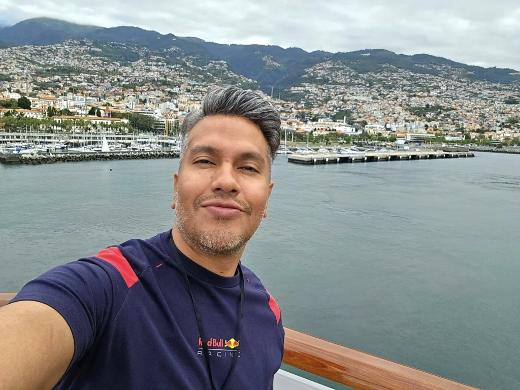 Cruising with Danny and Peter, Holland America Line, Nieuw Statendam, Funchal, Madeira. Portugal, History Adventure | A vibrant collage capturing a day in Funchal, Madeira: a sleek trike navigates winding roads with lush green hills in the background; the panoramic view from Pico dos Barcelos showcases Funchal Bay and the Desertas Islands under a clear sky; Cascata dos Anjos waterfall cascades from cliffs onto a road, surrounded by verdant greenery; Praia da Madalena do Mar’s pebbled beach and black volcanic sand meet gentle waves with towering cliffs above; the misty Valley of the Nuns nestles between rugged mountains, dotted with stone houses and chestnut groves; Cabo Girão’s glass-bottomed skywalk reveals a dizzying drop to the Atlantic and terraced fields below; a plate of warm bolo do caco flatbread filled with steak sits on a café table in Funchal’s colorful old town; the CR7 Museum displays Cristiano Ronaldo’s trophies and jerseys with a waterfront view of the Nieuw Statendam; and Nami Sushi Bar’s elegant sushi platter gleams under soft lighting aboard the ship.