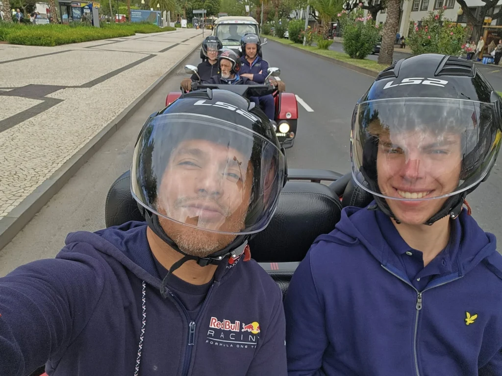Cruising with Danny and Peter, Holland America Line, Nieuw Statendam, Funchal, Madeira. Portugal, History Adventure | A vibrant collage capturing a day in Funchal, Madeira: a sleek trike navigates winding roads with lush green hills in the background; the panoramic view from Pico dos Barcelos showcases Funchal Bay and the Desertas Islands under a clear sky; Cascata dos Anjos waterfall cascades from cliffs onto a road, surrounded by verdant greenery; Praia da Madalena do Mar’s pebbled beach and black volcanic sand meet gentle waves with towering cliffs above; the misty Valley of the Nuns nestles between rugged mountains, dotted with stone houses and chestnut groves; Cabo Girão’s glass-bottomed skywalk reveals a dizzying drop to the Atlantic and terraced fields below; a plate of warm bolo do caco flatbread filled with steak sits on a café table in Funchal’s colorful old town; the CR7 Museum displays Cristiano Ronaldo’s trophies and jerseys with a waterfront view of the Nieuw Statendam; and Nami Sushi Bar’s elegant sushi platter gleams under soft lighting aboard the ship.