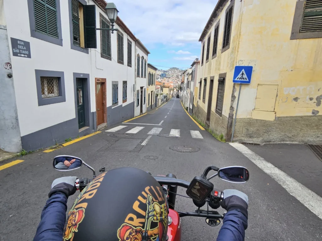 Cruising with Danny and Peter, Holland America Line, Nieuw Statendam, Funchal, Madeira. Portugal, History Adventure | A vibrant collage capturing a day in Funchal, Madeira: a sleek trike navigates winding roads with lush green hills in the background; the panoramic view from Pico dos Barcelos showcases Funchal Bay and the Desertas Islands under a clear sky; Cascata dos Anjos waterfall cascades from cliffs onto a road, surrounded by verdant greenery; Praia da Madalena do Mar’s pebbled beach and black volcanic sand meet gentle waves with towering cliffs above; the misty Valley of the Nuns nestles between rugged mountains, dotted with stone houses and chestnut groves; Cabo Girão’s glass-bottomed skywalk reveals a dizzying drop to the Atlantic and terraced fields below; a plate of warm bolo do caco flatbread filled with steak sits on a café table in Funchal’s colorful old town; the CR7 Museum displays Cristiano Ronaldo’s trophies and jerseys with a waterfront view of the Nieuw Statendam; and Nami Sushi Bar’s elegant sushi platter gleams under soft lighting aboard the ship.