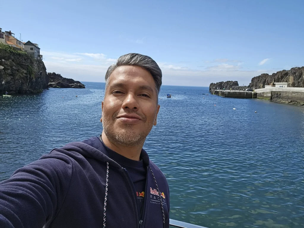 Cruising with Danny and Peter, Holland America Line, Nieuw Statendam, Funchal, Madeira. Portugal, History Adventure | A vibrant collage capturing a day in Funchal, Madeira: a sleek trike navigates winding roads with lush green hills in the background; the panoramic view from Pico dos Barcelos showcases Funchal Bay and the Desertas Islands under a clear sky; Cascata dos Anjos waterfall cascades from cliffs onto a road, surrounded by verdant greenery; Praia da Madalena do Mar’s pebbled beach and black volcanic sand meet gentle waves with towering cliffs above; the misty Valley of the Nuns nestles between rugged mountains, dotted with stone houses and chestnut groves; Cabo Girão’s glass-bottomed skywalk reveals a dizzying drop to the Atlantic and terraced fields below; a plate of warm bolo do caco flatbread filled with steak sits on a café table in Funchal’s colorful old town; the CR7 Museum displays Cristiano Ronaldo’s trophies and jerseys with a waterfront view of the Nieuw Statendam; and Nami Sushi Bar’s elegant sushi platter gleams under soft lighting aboard the ship.