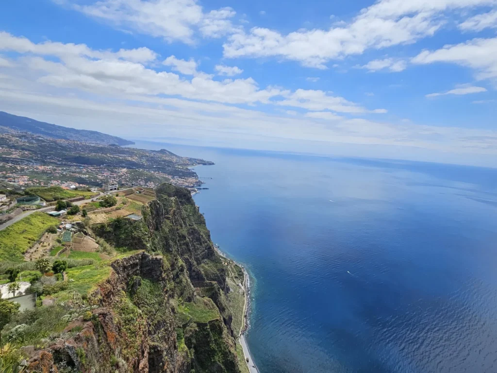 Cruising with Danny and Peter, Holland America Line, Nieuw Statendam, Funchal, Madeira. Portugal, History Adventure | A vibrant collage capturing a day in Funchal, Madeira: a sleek trike navigates winding roads with lush green hills in the background; the panoramic view from Pico dos Barcelos showcases Funchal Bay and the Desertas Islands under a clear sky; Cascata dos Anjos waterfall cascades from cliffs onto a road, surrounded by verdant greenery; Praia da Madalena do Mar’s pebbled beach and black volcanic sand meet gentle waves with towering cliffs above; the misty Valley of the Nuns nestles between rugged mountains, dotted with stone houses and chestnut groves; Cabo Girão’s glass-bottomed skywalk reveals a dizzying drop to the Atlantic and terraced fields below; a plate of warm bolo do caco flatbread filled with steak sits on a café table in Funchal’s colorful old town; the CR7 Museum displays Cristiano Ronaldo’s trophies and jerseys with a waterfront view of the Nieuw Statendam; and Nami Sushi Bar’s elegant sushi platter gleams under soft lighting aboard the ship.