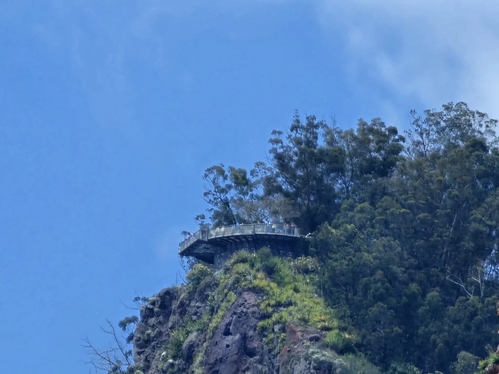 Cruising with Danny and Peter, Holland America Line, Nieuw Statendam, Funchal, Madeira. Portugal, History Adventure | A vibrant collage capturing a day in Funchal, Madeira: a sleek trike navigates winding roads with lush green hills in the background; the panoramic view from Pico dos Barcelos showcases Funchal Bay and the Desertas Islands under a clear sky; Cascata dos Anjos waterfall cascades from cliffs onto a road, surrounded by verdant greenery; Praia da Madalena do Mar’s pebbled beach and black volcanic sand meet gentle waves with towering cliffs above; the misty Valley of the Nuns nestles between rugged mountains, dotted with stone houses and chestnut groves; Cabo Girão’s glass-bottomed skywalk reveals a dizzying drop to the Atlantic and terraced fields below; a plate of warm bolo do caco flatbread filled with steak sits on a café table in Funchal’s colorful old town; the CR7 Museum displays Cristiano Ronaldo’s trophies and jerseys with a waterfront view of the Nieuw Statendam; and Nami Sushi Bar’s elegant sushi platter gleams under soft lighting aboard the ship.